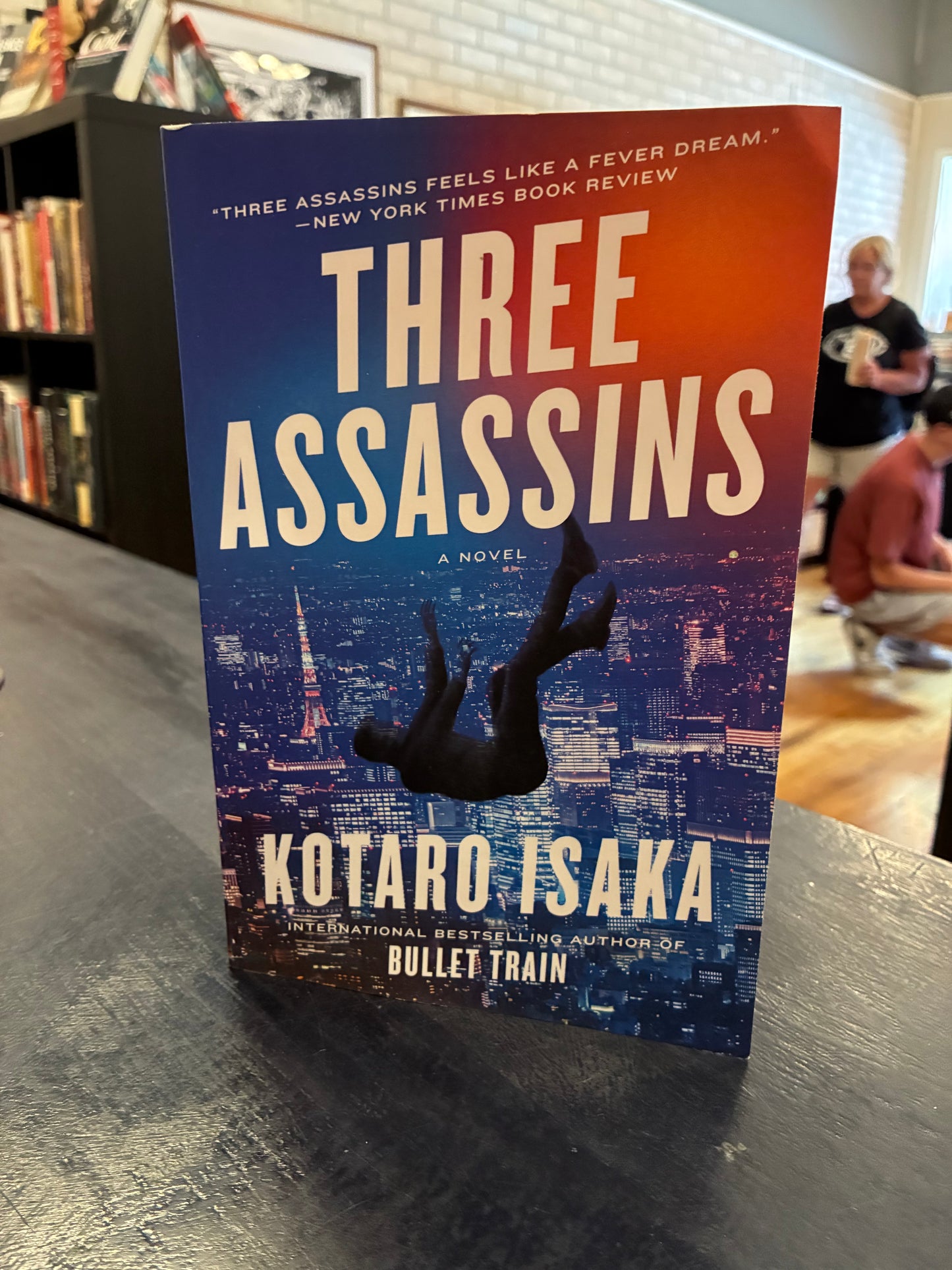 Book titled 'Three Assassins' by Kotaro Isaka on a surface with blurred background