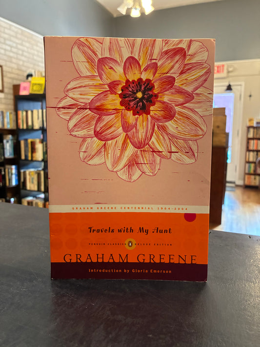 Travels with My Aunt' by Graham Greene, featuring a large pink and orange flower illustration on the cover, displayed on a dark tabletop in a bookstore setting.