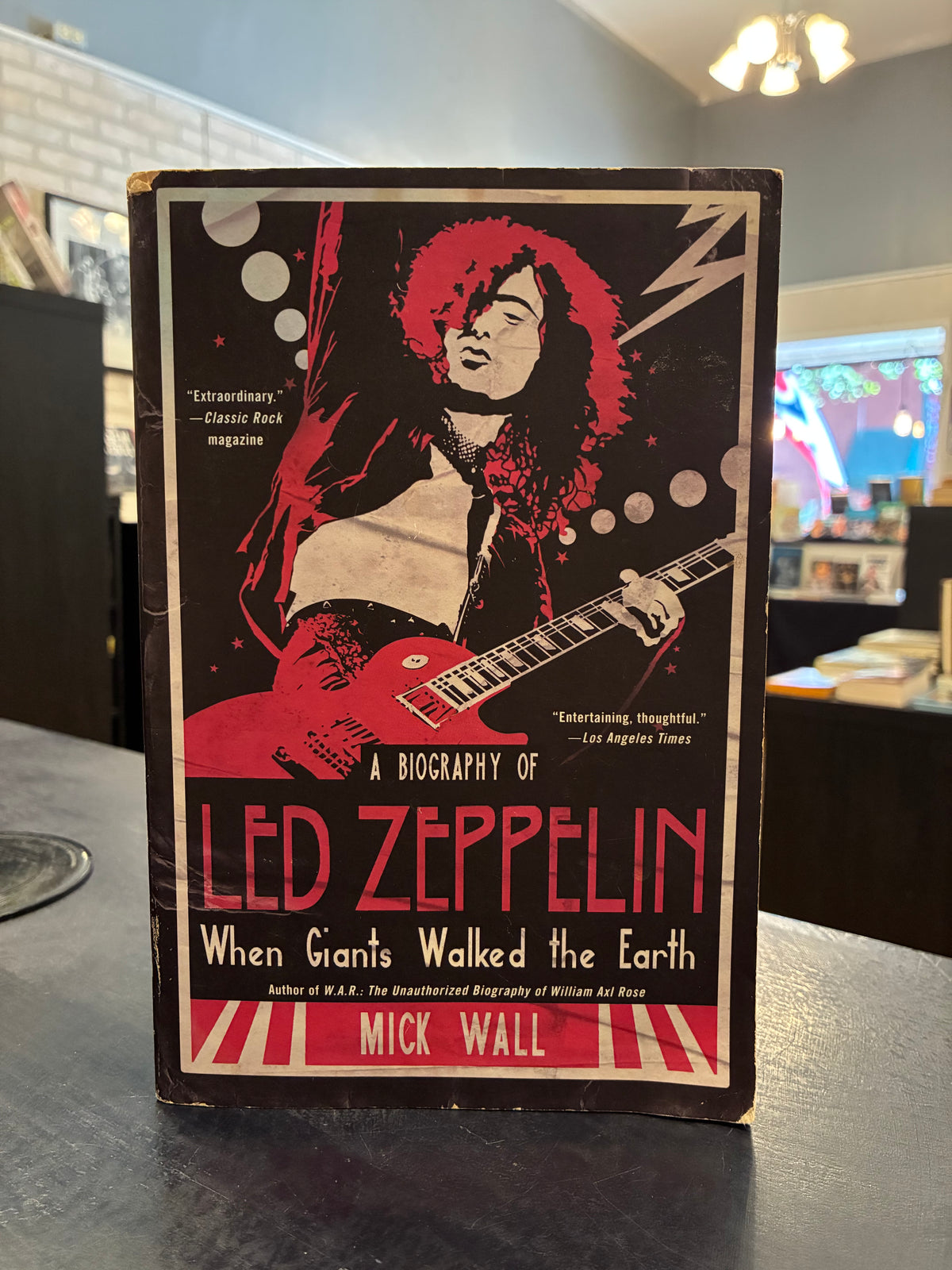 book titled 'A Biography of Led Zeppelin: When Giants Walked the Earth' by Mick Wall, featuring a bold red and black cover illustration of a guitarist, photographed standing on a dark tabletop in an indoor setting.
