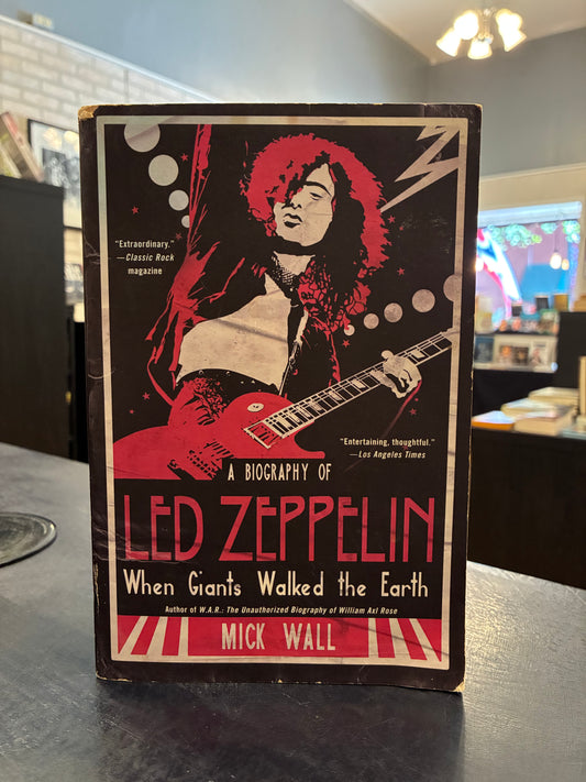 book titled 'A Biography of Led Zeppelin: When Giants Walked the Earth' by Mick Wall, featuring a bold red and black cover illustration of a guitarist, photographed standing on a dark tabletop in an indoor setting.