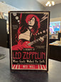 book titled 'A Biography of Led Zeppelin: When Giants Walked the Earth' by Mick Wall, featuring a bold red and black cover illustration of a guitarist, photographed standing on a dark tabletop in an indoor setting.